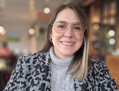 Portret van een glimlachende vrouw met een leeuwprint jas en een grijze trui, zittend in een cafe.