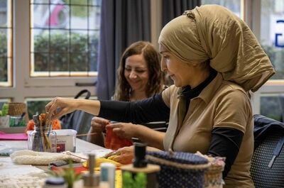 Twee vrouwen ontspannen met handwerk in een lichte, gezellige ruimte, met materialen en gereedschappen om hen heen.