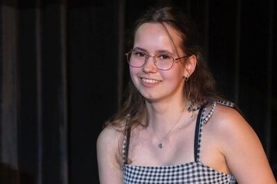 Jongeman met een glimlach, gekleed in een zwart-wit geruite top, staat op een podium met een donkere achtergrond.